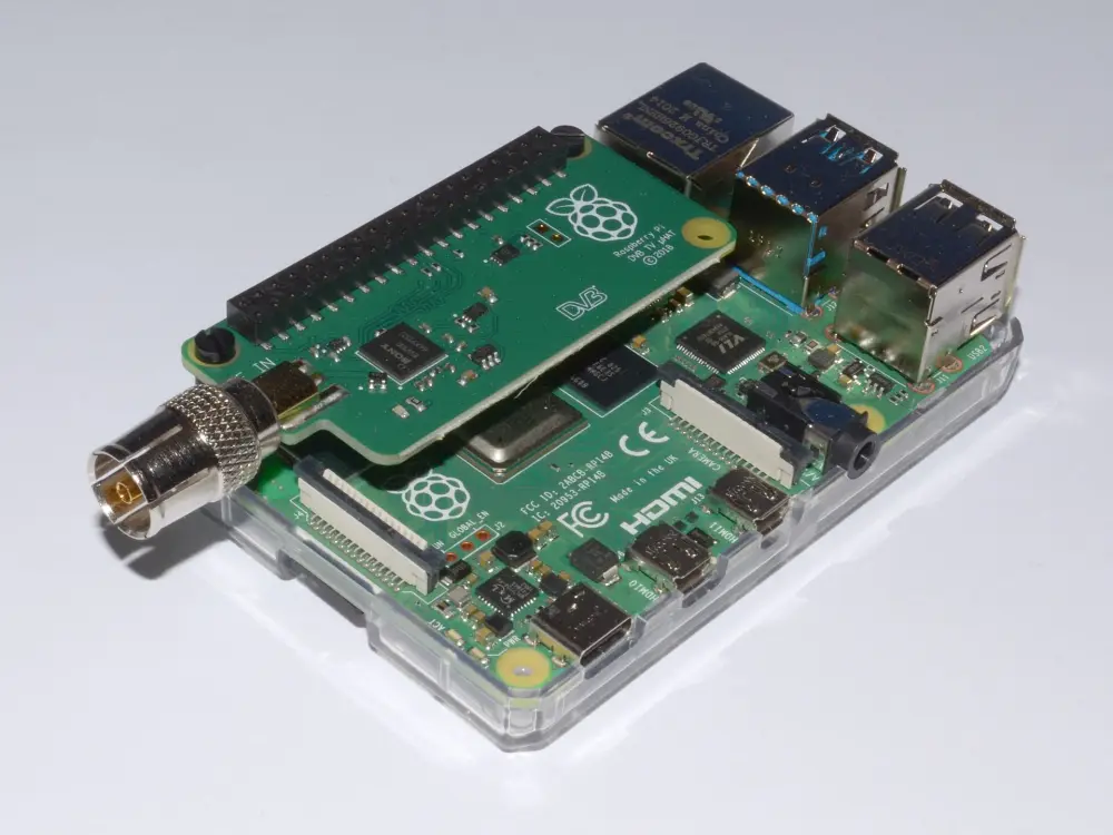 A Raspberry Pi 4 in a clear case with a small TV tuner board fitted on top and an aerial socket at its edge